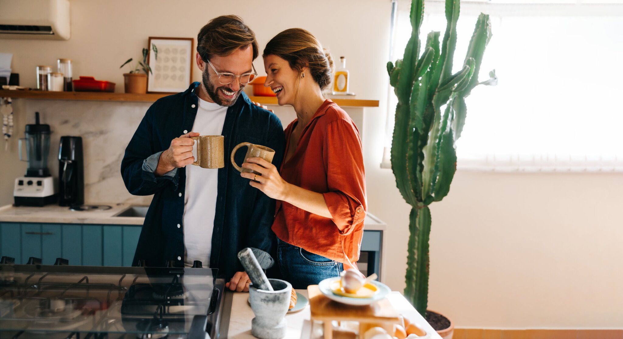 young couple standing in kitchen laughing together, drinking coffee.